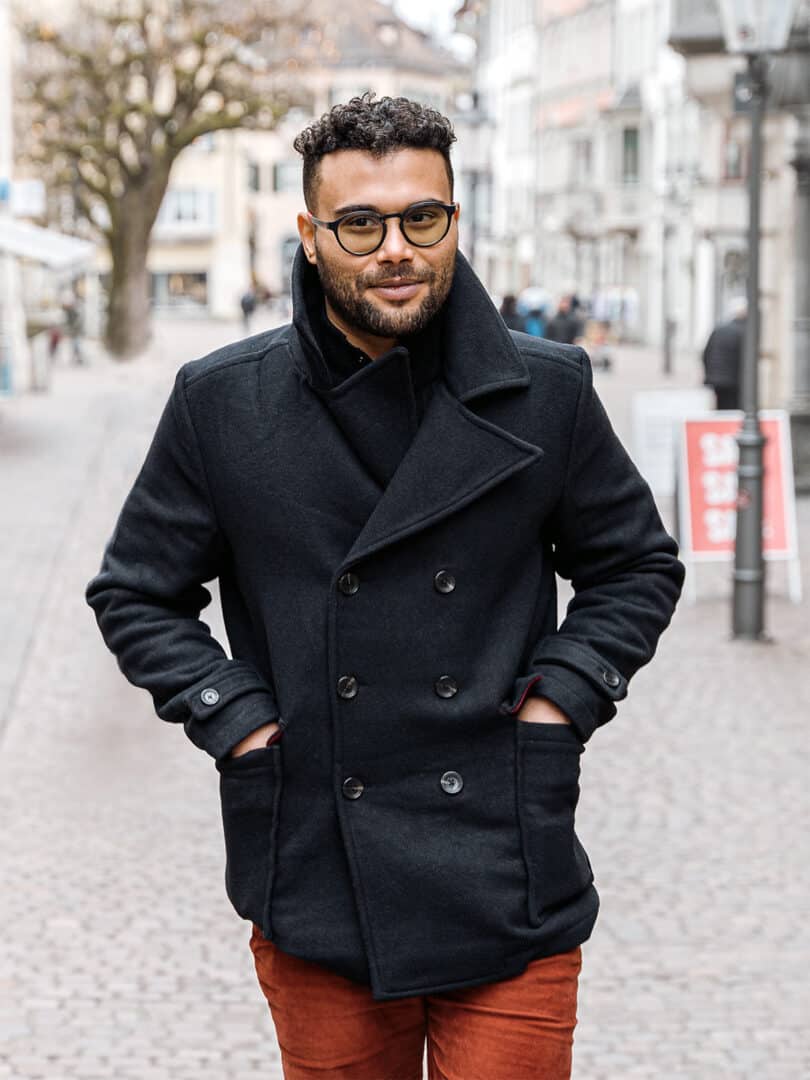 Uomo con cappotto doppio petto nero, mani in tasca, in contesto cittadino invernale